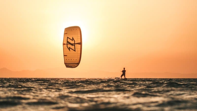 Kiteboarder riding across calm blue water under a clear sky