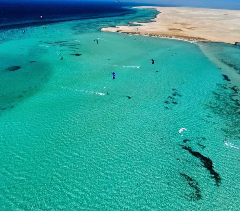 Aerial view of kites flying over a shallow turquoise Red Sea sandbar lagoon