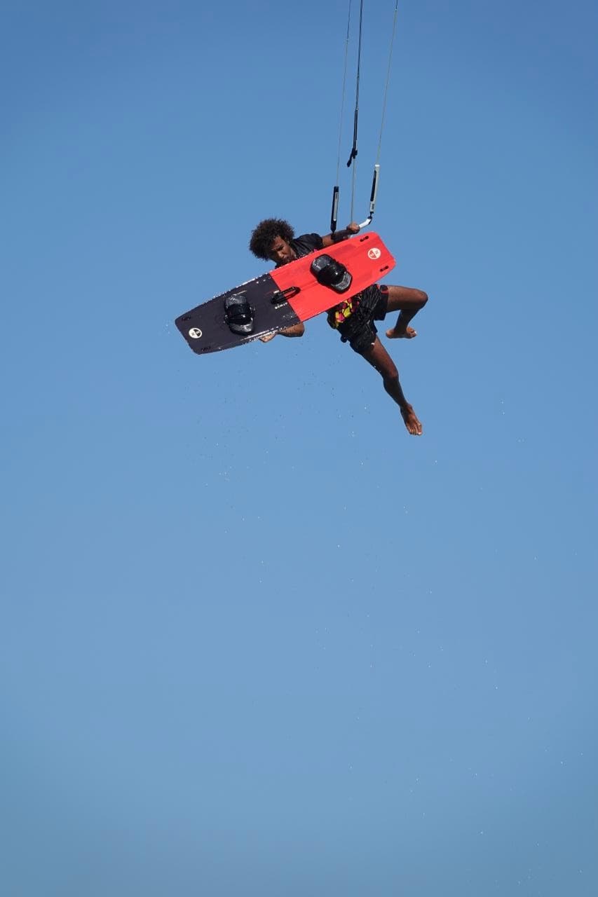 Anubis Kite rider grabbing the board mid-jump against a clear Red Sea sky
